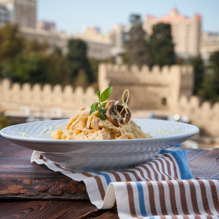 Vitalitaly Spaghetti com queijo e cogumelos em prato branco sobre mesa de madeira escura com vista para a cidade — Massa italiana artesanal bronzeada para receitas premium